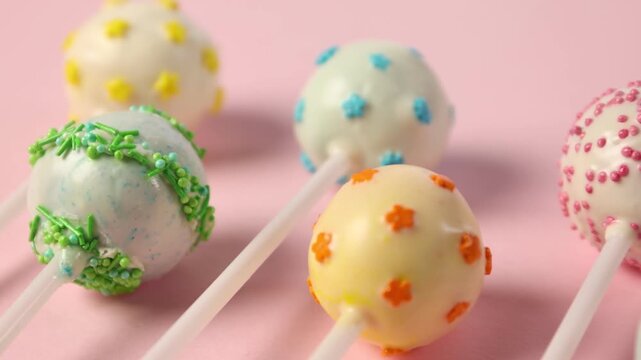 Tasty cake pops on pink background, closeup. Camera moving left