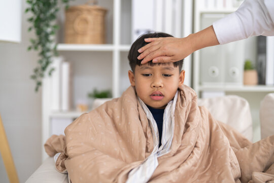 Mother hand touching sick asian boy forehead checking high fever temperature, home pediatric health care, flu symptoms, rsv, influenza, pneumonia, bronchitis illness and hand foot mouth disease