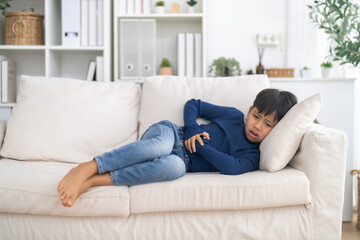 Obraz premium Portrait of sick unhappy little child asian boy touching belly stomach with suffering from stomach ache pain, gastritis, gastroenteritis, food poisoning, diarrhea, intestinal inflammation at home