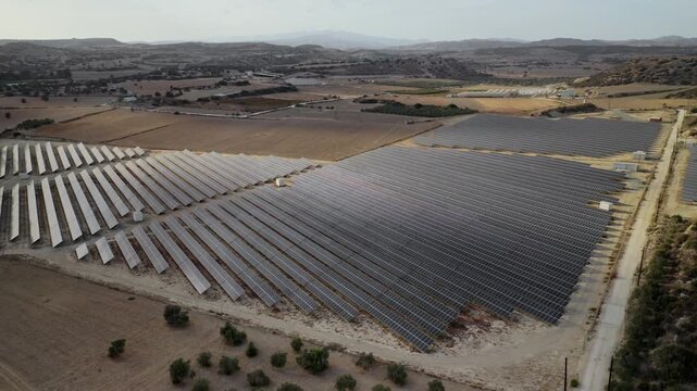 Extensive solar farm covering a large area of fields and hills in Cyprus, capturing sunlight for sustainable energy production and contributing to environmental conservation. Aerial view drone flight