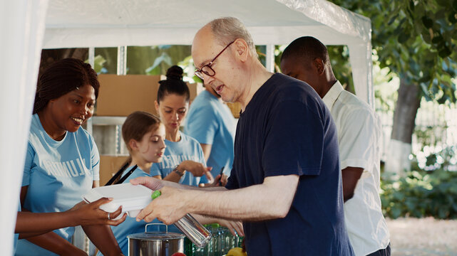 Friendly volunteers offering hunger relief to poor and needy individuals, people of different ethnicities who are less fortunate and homeless are fed by a charitable organization.
