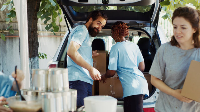Poor, needy and homeless people are helped by charity workers at a non-profit food drive program, donation boxes are provided to the less fortunate by young multiethnic volunteers.