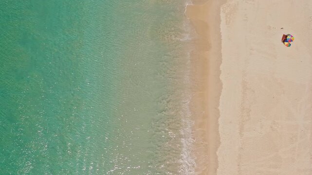 Phuket tropical beach, clear turquoise sea water, golden sand. Gentle waves breaking on shore, colorful beach umbrella on expansive coastline. Summer vacation travel background. Aerial top down view