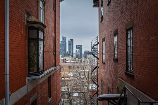 View of Montreal skyline and downtown CBD from between red brick residential buildings, showing urban housing, business towers and real estate density in a North American city in Quebec and Canada.