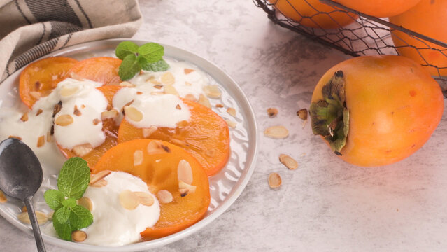 Sliced persimmon dessert with yogurt mint and almond flakes on a ceramic plate