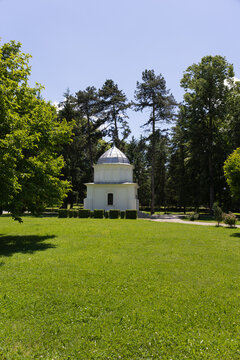 small white pavilion with a metal dome surrounded by green trees and grass lawn in a park under a blue sky on a bright sunny day
