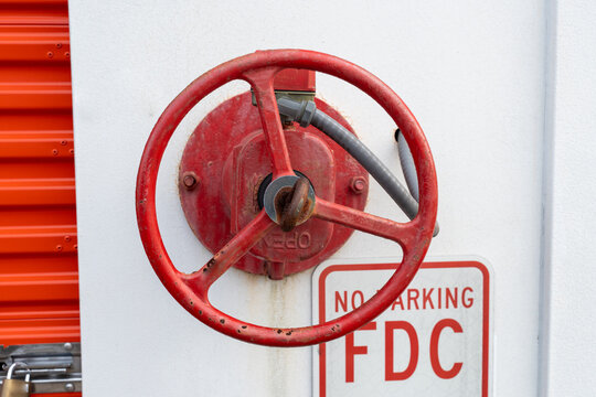 a red metal wheel of a red fire department connection (FDC) valve mounted on a wall above a "No Parking FDC" sign, highlighting fire protection infrastructure, emergency access 