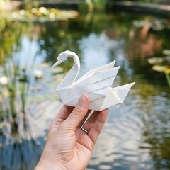 Obraz premium hand holding an elegant origami swan gracefully gliding on water, 