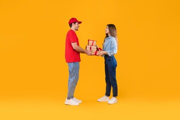 Obraz premium Smiling Man And Woman Exchanging Gifts In Cheerful Manner At Bright Yellow Background, Holding Wrapped Presents Together, Celebrating Joyful Occasion, Festivity Concept.