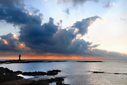 Dramatic sunset with rays of light over the coast and lighthouse in Jeju Island, South Korea