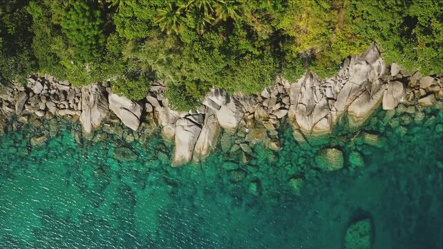 Turquoise ocean water gently splashing against a rocky coastline with lush green tropical vegetation framing the top of the scene in Phuket, Thailand. Natural background. Aerial top down view shot