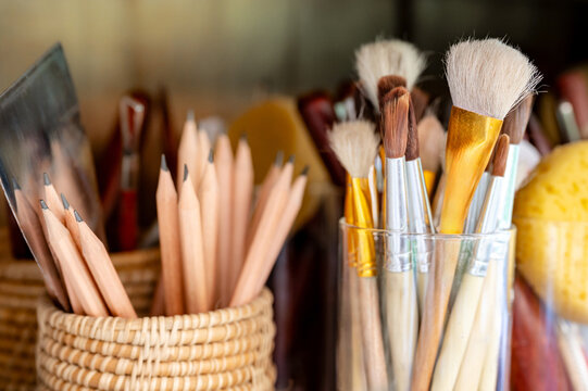 Various artist paintbrush with pencils, painting spatula and sponge grouping in the glass holder in art workshop studio. Art paint tools supplies for creativity class