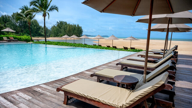 Luxury resort hotel with swimming pool and beach chairs or loungers under umbrellas. Tropical beach landscape in sunny day. Summer vacation and holiday travel concepts