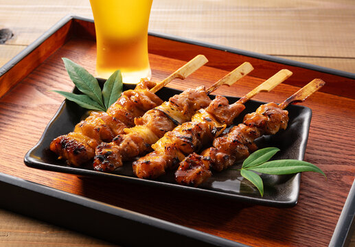 Japanese Yakitori Chicken Skewers with Blurred Glass of Beer on Wooden Tray
