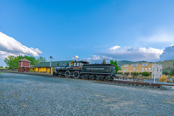 A historic black steam locomotive parked on the tracks outside the depot at the Nevada State Railroad Museum under a cloudy sky. © ZL Visuals