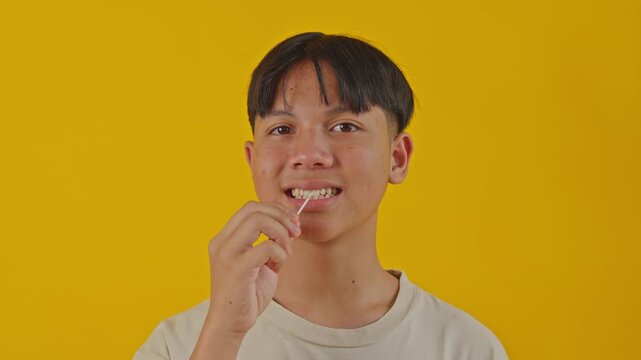 Asian teenager using toothpick to clean teeth isolated on yellow background