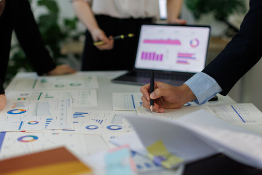 Businesswoman presenting data analytics on a laptop to colleagues during a corporate meeting, showing financial graphs and charts for strategic planning and growth in an office setting