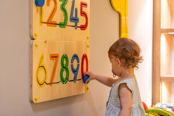 Toddler girl playing with busy board with numbers on the wall. Educational toys. Busy board for children. Wooden game board with numbers © Maria