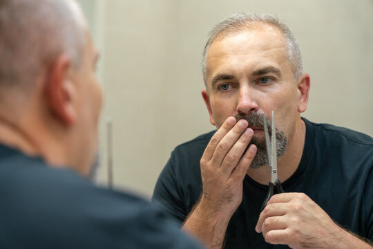 Middle-aged handsome man using scissors to cut his beard a litlie and fix the shape