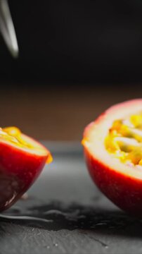 ripe passion fruit being sliced in half in close-up, knife glides through wrinkled purple skin as camera descends toward the center, revealing glossy pulp, seeds with rich tropical texture