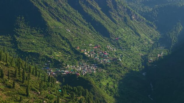 Grahan Village with clustered homes, terraced hillsides, dense pine forests, and steep Himalayan mountain slopes in Parvati Valley near Kasol, Himachal Pradesh, India. Drone aerial establishing shot