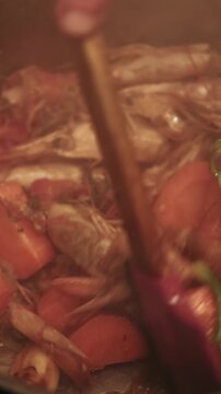 Vertical video. Cooking seafood. Shrimp shells. Chef hand stirring fried ingredients for bisque soup. Tom yum kung with carrots green herbs spices in hot steaming pot.