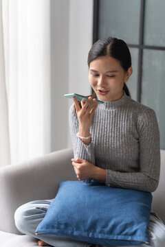 Asian woman using voice assistant on smartphone at home conversation with online assistant&nbsp;Voice chat bot conversational AI Modern Technologies.