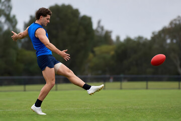 Naklejka premium AFL Player Kicking Football on Grassy Oval