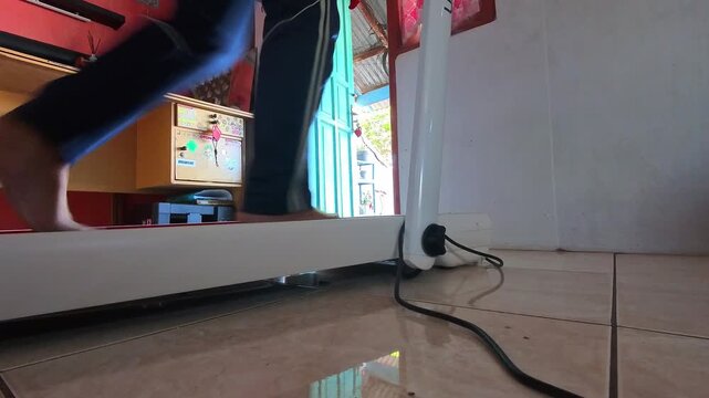 Time Lapse Video of Person standing and walking on treadmill on tiled floor. Foot moves near base as power cord connects to outlet. Simple indoor scene with modest home surroundings. 4K Time Lapse