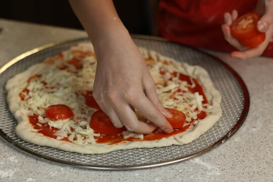 The process of making homemade pizza: a woman's hands arrange slices of fresh tomatoes and peppers onto a pizza base that has already been sprinkled with cheese. The images feature a cozy home or culi