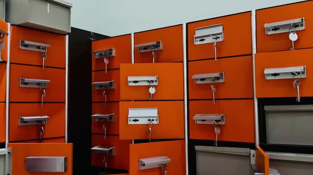 Rows of bright orange metal safety deposit locker boxes with keys in the locks. Secure luggage storage lockers, postal mailboxes, or bank vault box terminal for safe keeping valuable properties.