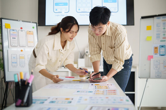 UX designers collaborating on mobile app prototype testing, comparing smartphone screens with printed wireframes in a modern office.