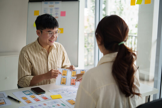 UX UI designers collaborating on smartphone application layout, reviewing paper prototypes during a casual business meeting.