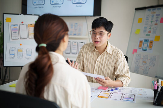 UX UI designers collaborating on smartphone application layout, reviewing paper prototypes during a casual business meeting.