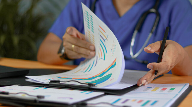 Healthcare professional reviewing medical reports and statistical charts in a clinical setting. Close-up of healthcare analytics, patient data management, medical research, hospital administration