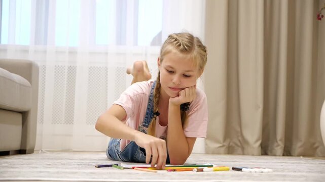 Cute preteen girl lying on floor and drawing on paper in living room