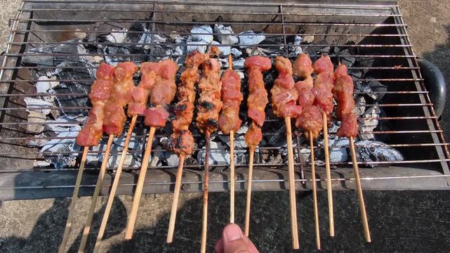 Video of Grilled skewers sizzle over glowing charcoal. Hand adjusts and flips skewers near a smoky barbecue grill. Sunlight casts shadows on the ground. Ideal for outdoor cooking. Footage Family Barbe