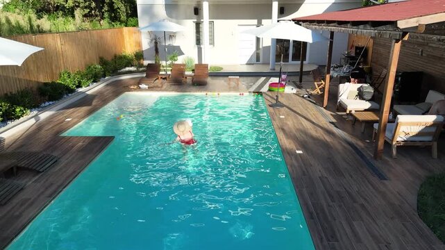 Mother and baby enjoying playtime in outdoor swimming pool surrounded by greenery on a sunny day