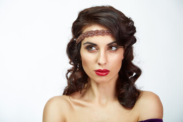 Fototapeta premium Woman with dark, wavy hair poses against a plain white backdrop. She wears a deep purple off-shoulder velvet dress. Her metallic headband adds intricate detail to her look
