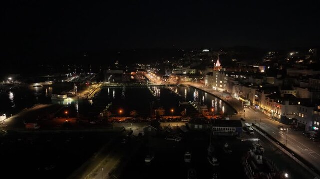 St Peter Port Guernsey at night.High forward drone footage over QEII Marina and harbour with ights reflecting in calm water and vibrant night time townscape beyond
