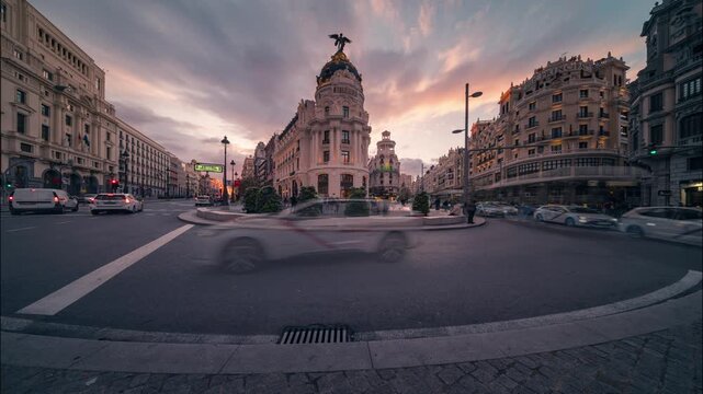 Day-to-night timelapse of the iconic Metropolis Building in Madrid. Colorful sunset skies transition into city lights as traffic and pedestrians move through the historic city center.
