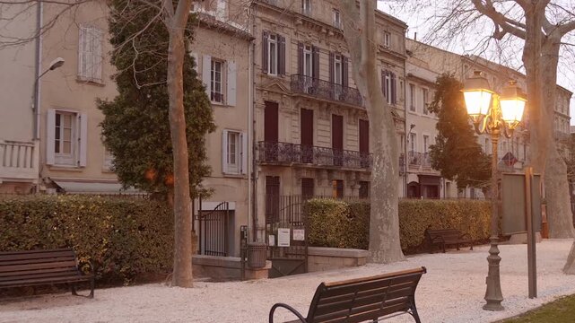 Empty benches and vintage streetlamp line a quiet tree-shaded walkway at dusk