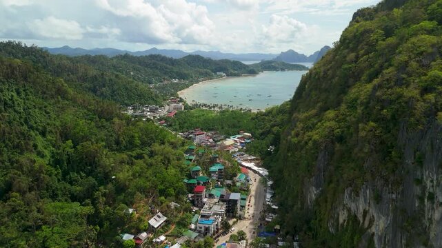 Aerial flyover above Taytay El Nido National Highway through town between limestone cliffs with curvy Corong Corong Beach and bay of El Nido Palawan Philippines