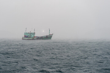 Fototapeta premium Traditional Thai Fishing Boat Navigating Through Heavy Rain and Rough Seas in the Gulf of Thailand. A weathered local fishing boat travels across choppy ocean waters during heavy rain in Thai sea.