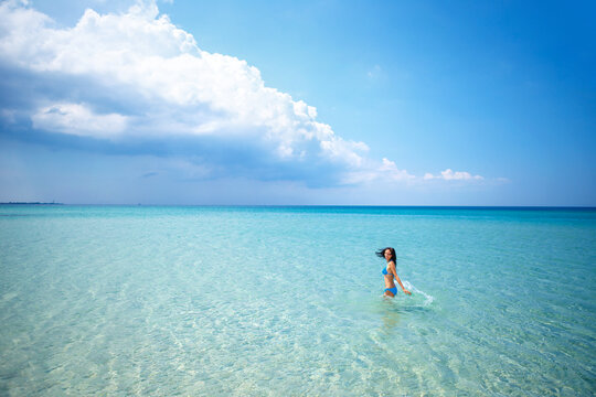 Caucasian Brunette Slim Woman in Blue Bikini Standing in Tropical Turquoise Sea under Cloud Wide Beach View