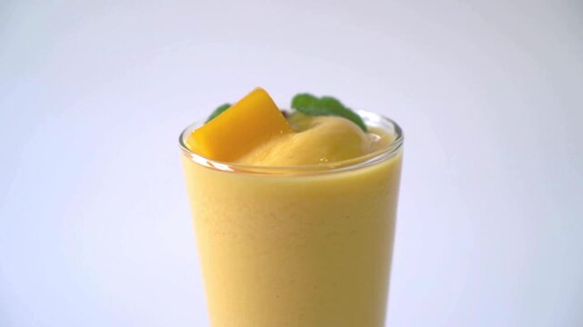 Fresh mango smoothie in glass with mint leaf, tropical fruit shake on white background, healthy yellow mango lassi drink for summer refreshment