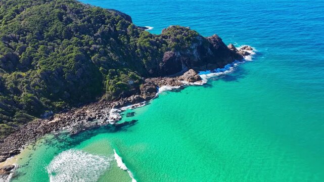 Aerial video panning around Charlotte Head at Boomerang Beach near Pacific Palms, NSW, Australia. The sweeping camera movement showcases the rugged rocky headland, clear turquoise waters
