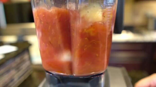 Fresh tomatoes, garlic, and onions are being blended into a smooth sauce inside a kitchen blender.
