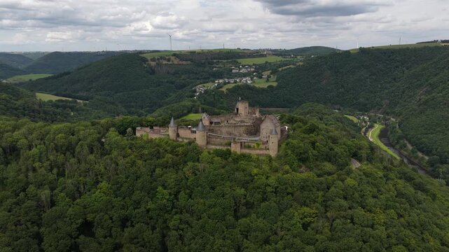 Drone footage slowly revealing the historic bourscheid castle, a magnificent medieval fortress nestled atop a hill surrounded by a lush green forest and the sure river valley in luxembourg