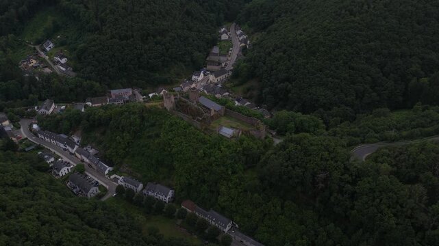 Cinematic aerial footage capturing the historic ruins of esch sur sure castle and the charming village nestled in the green, wooded valley of the upper sure nature park in luxembourg